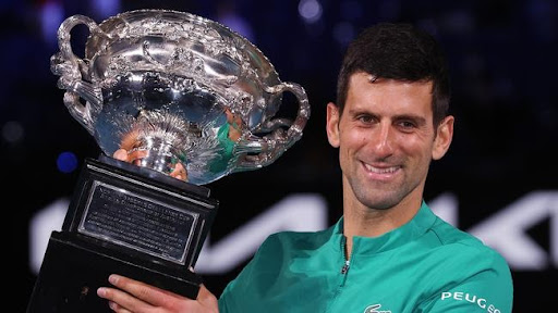 A victorious Novak Djokovic hoists the 2021 Australian Open men's singles championship trophy. This was his ninth win at the tournament, one year before he was barred from returning to defend this title. 