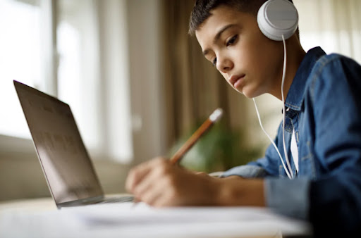 A focused teenage boy working on homework while listening to music through headphones.